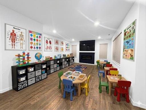 A bright classroom with learning posters, cubby storage, and small colorful chairs around a table