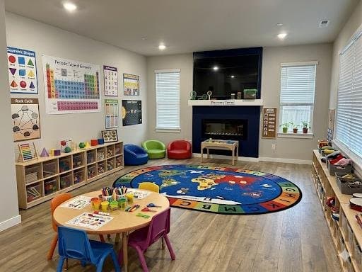 A discovery room with a large alphabet rug, reading nook chairs, and science learning charts