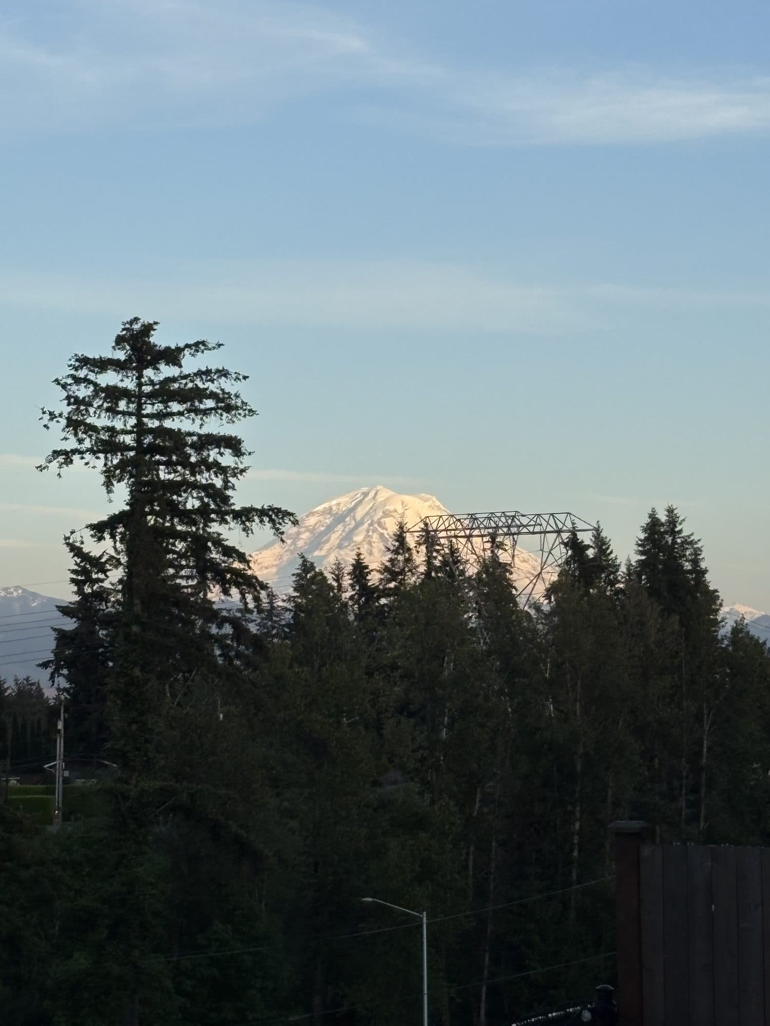 Mount Rainier at dusk, snow-capped and framed by evergreens, seen from the school's deck